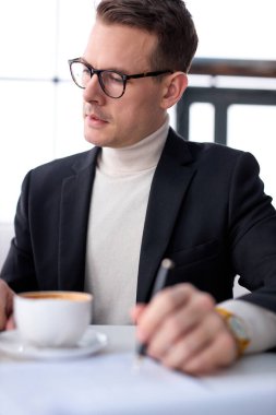 İş adamı gözlüklü bir erkek iş planı yazıyor, not alıyor, restoranda masada oturuyor.