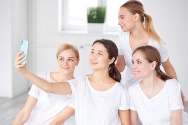 Beden eğitimi sırasında cep telefonuyla fotoğraf çeken alımlı ve mutlu kadınların yan görüntüsü