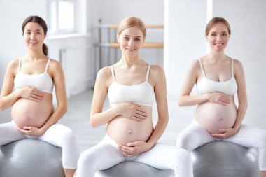 Güzel görünümlü, karnı çıplak hamile kadınlar perinatal jimnastik yaparken spor toplarının üzerine otururlar.
