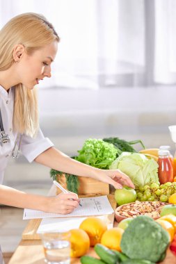 Genç Diyetisyen diyet diyet planının yan görünüşü. Farklı sağlıklı ürünlerle dolu bir masa.