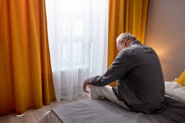 Evde yatakta oturan üzgün yaşlı adamın dikiz aynası.