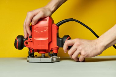 Tanımlanamayan bir erkeğin sarı arka planda elektrikli testereyi açması