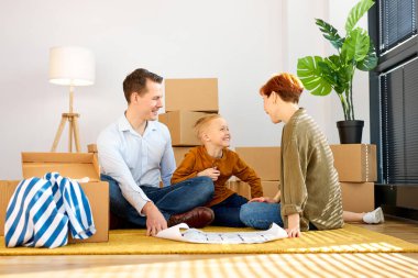 Yeni evdeki karton kutuların arasında yerde oturan çocukla mutlu ve pozitif bir aile.