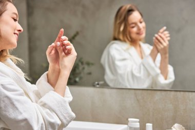 Bornozlu güzel bir kadın banyoda krem sürdükten sonra cilt bakımının keyfini çıkarıyor.