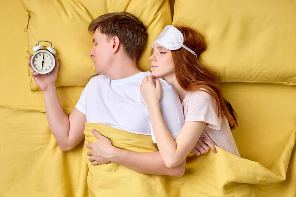 top view on couple lying in bedroom. man holds alarm clock near ear