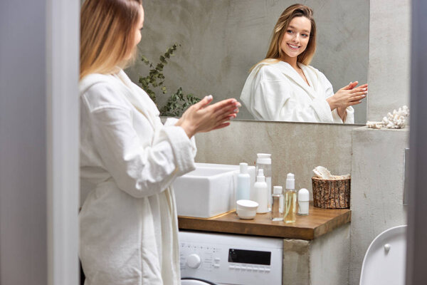 Красивая женщина использует средства по уходу за кожей дома в светлой ванной комнате