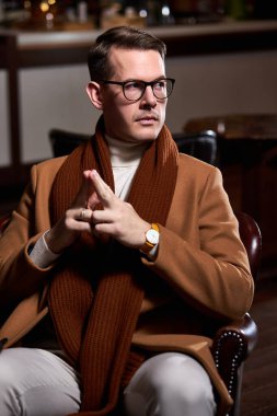 Zarif ceketli bir yönetici restoranda oturur düşüncelerine odaklanır ve yan gözle bakar.