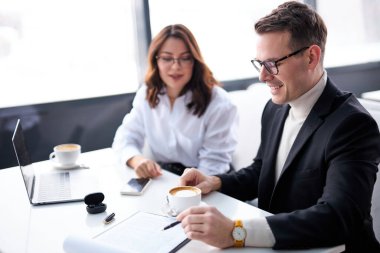 İki işçi masanın arkasında oturup konuşuyorlar, pano dökümanlarını kullanıyorlar, tartışıyorlar.