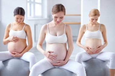 Koca göbekli bir grup ağır kadın spor toplarının üzerine oturup rahatlıyorlar.