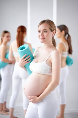 Koca göbekli, bebek bekleyen, spor salonunda poz veren sarışın bir bayan.