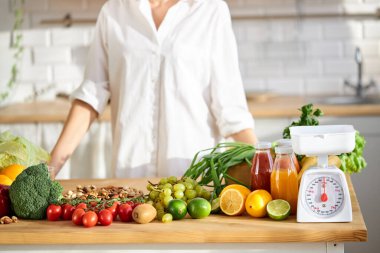 Kesilmiş kadın taze ürünlerle masanın başında duruyor.