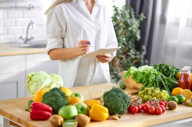 Tanımlanamayan kadın beslenme uzmanı mutfakta deftere yazıyor.