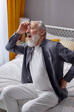 Emekli adam evde sırt ağrısı çekiyor, yataktan kalkmakta zorlanıyor.