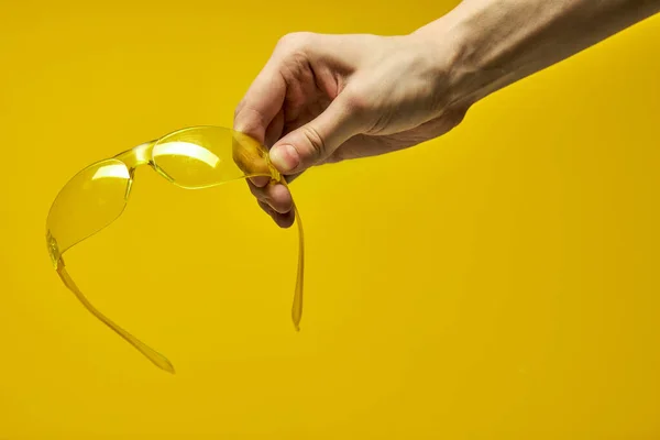 unrecognizable male holding yellow protective spectacles on yellow background isolated