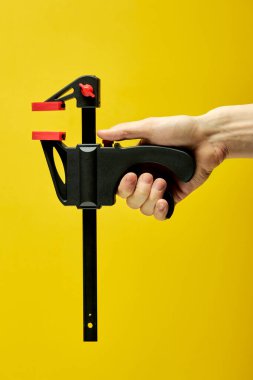 Erkek ellerindeki C-klemp sarı arka planda izole edilmiş.