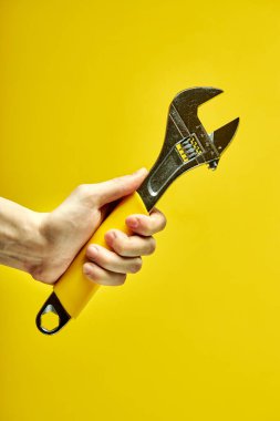 Sarı arka planda izole edilmiş kırpılmış erkek ellerindeki Ayarlanabilir Anahtarın yakın plan görüntüsü