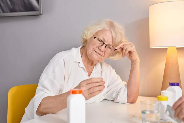 Femme âgée avec des médicaments dans les mains lecture prescription de médicaments, assis seul à la maison — Photo