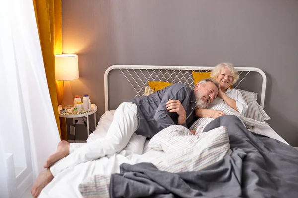 Positive kaukasische ältere Paare haben Spaß. Lachen, wenn man zu Hause im Bett liegt — Stockfoto