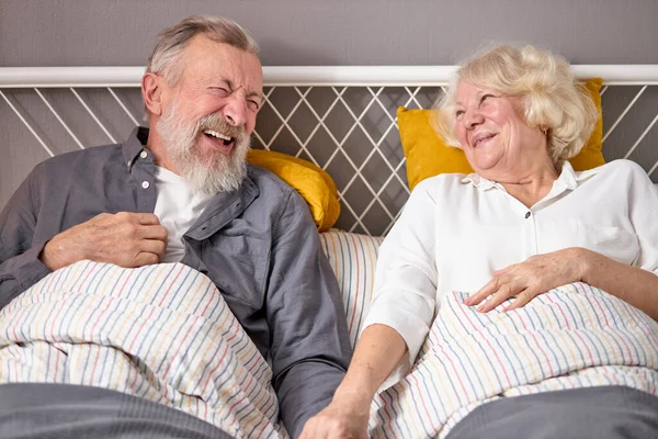 Casal de idosos caucasianos positivos se divertir. rir enquanto deitado na cama em casa — Fotografia de Stock