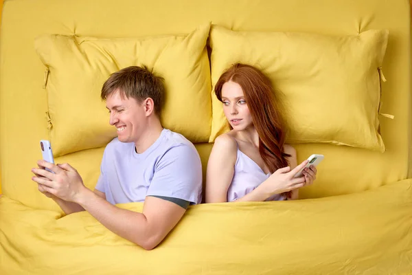 married couple lying back to back in bed and using smartphones at night, have rest