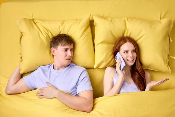 Entfremdetes Millennial-junges Paar im Bett, Frau spricht über Phome With Someon, Achten Sie auf Ehemann — Stockfoto