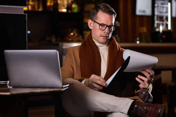 Pohledný podnikatel v elegantním kabátě sedí na křesle s notebookem a tabletem — Stock fotografie