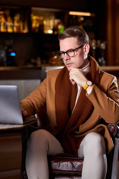 Уверенный бизнесмен сидит, думая о деловых сделках и планах, используя ноутбук, в холле гостиницы — стоковое фото