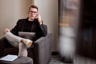 Otel odasında bilgisayarla çalışan genç işadamı, oturup kablosuz kulaklıkla bilgi dinliyor.