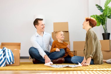 Çocukla rahat bir aile yerde oturup konuşur, evlerini planlar, yeni bir daireye taşınırlar.