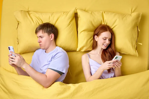 couple lying back to back in bed and using smartphones at night, have rest