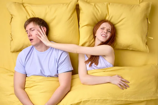 Der Kopf eines jungen Paares im Bett. Schöne rothaarige Frau wütend auf schlafenden Ehemann — Stockfoto