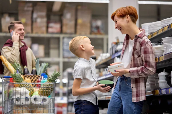 Menino bonito pedir mãe para comprar belos pratos na loja — Fotografia de Stock