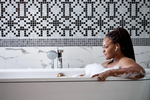 Home Spa And Relax On Weekends. Афроамериканка в ванной с пеной наслаждается купанием в ванной — стоковое фото