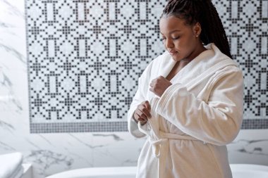 Beyaz bornozlu çekici afro kadın banyo yapmaya hazırlanıyor. Banyo prosedürleri