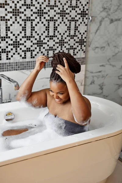 Домашняя спа и отдых на сорняках. Симпатичная американка из Африки в ванной с пеной наслаждается купанием в ванной комнате — стоковое фото