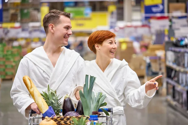 Gostando de fazer compras juntos. feliz jovem casal em roupão de banho de ligação uns com os outros e sorrindo enquanto caminha na loja — Fotografia de Stock