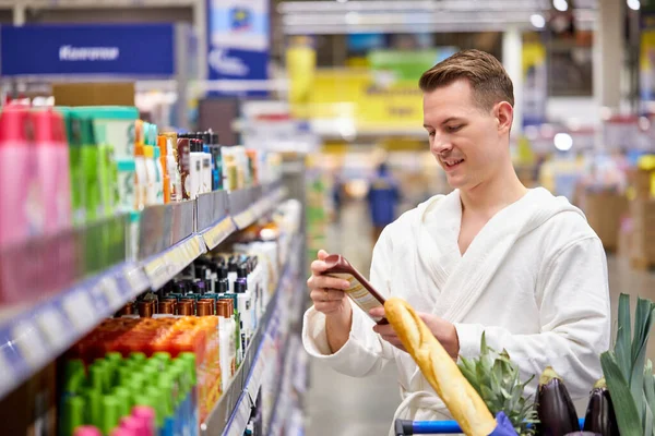 Handsome good-looking man need new shampoo or shower gel, came in supermarket in bathrobe