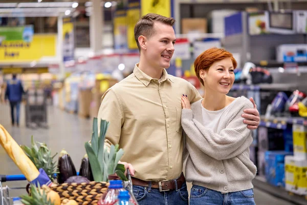 Rodzina dwojga dorosłych przytulających się w supermarkecie, cieszących się razem zakupami — Zdjęcie stockowe
