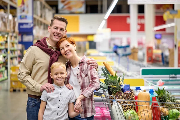 Retrato de jovem família europeia americana com filho pré-adolescente, carregando carrinho com compras depois de fazer compras no supermercado — Fotografia de Stock