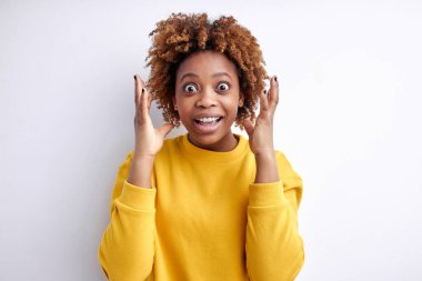 Mutlu Şoklar. Şaşkınlık içindeki genç siyahi kadın beyaz arka planda dikilirken, şok içinde kollarını açıyor.