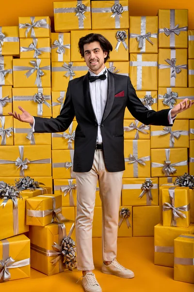 Agradable Afable caucásico morena chico en traje de negocios se para en el fondo lleno de regalos, sonriendo — Foto de Stock