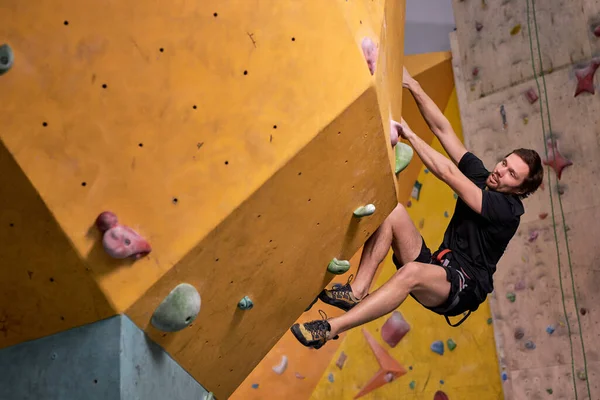 Jovem do sexo masculino sobe uma parede de rocha artificial, esporte e fitness conceito, vista lateral — Fotografia de Stock