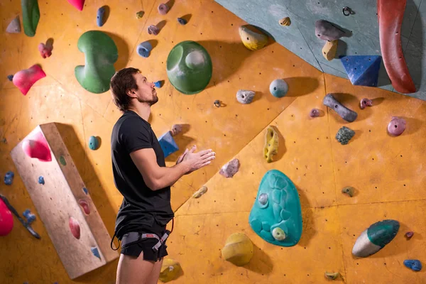 Vista lateral sobre o homem alpinista esporte profissional se preparando para treinar no ginásio na parede artificial — Fotografia de Stock