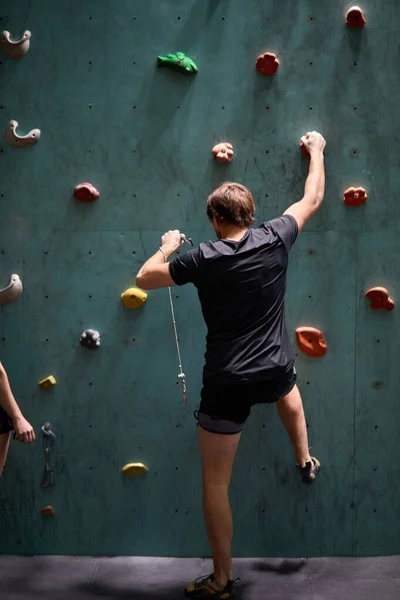 Pewny siebie mężczyzna alpinista wspinaczka sztuczna ściana skalna wewnątrz w centrum sportowym — Zdjęcie stockowe