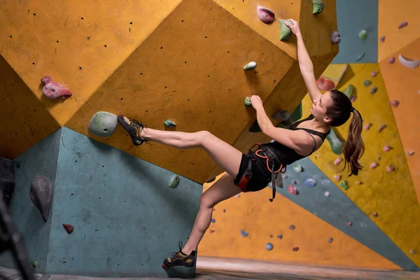 Спортсменка поднимается по крутой скале, взбирается на искусственную стену в помещении — стоковое фото