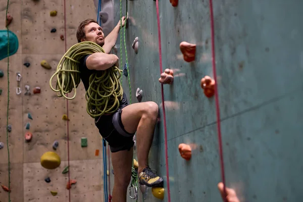 Спортсмен поднимается по крутой скале, взбирается на искусственную стену в помещении — стоковое фото