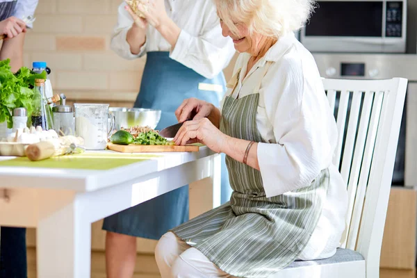 Side View Portrait Of Pleasant Smiling Aged Woman In Apron Chopping Ingredients Food