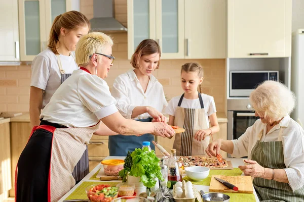 Семья веселится, делая пиццу вместе. бабушка на кухне с семьей, помогают друг другу — стоковое фото