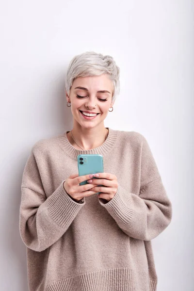 Portret van vrij korte harige vrouw in beige shirt chatten met een vriend met behulp van smartphone — Stockfoto