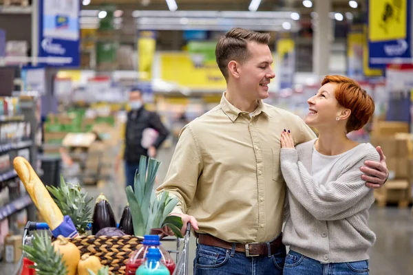 Χαμογελαστό ζευγάρι κοιταχτούν αγκαλιασμένοι, χαμογελαστοί, ερωτευμένοι ενώ ψωνίζουν στο σούπερ μάρκετ — Φωτογραφία Αρχείου